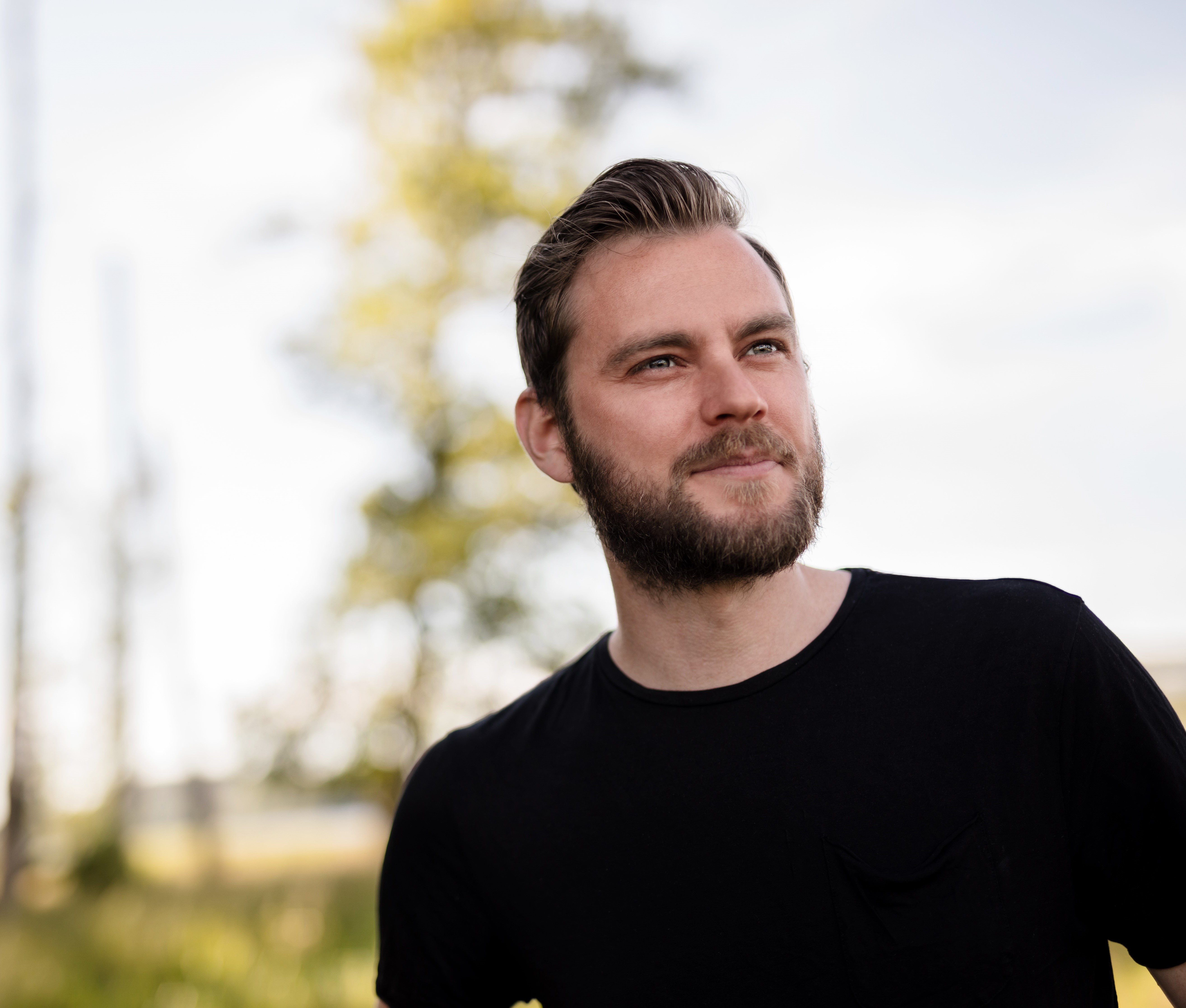 Man i 30 årsåldern, svart t-shirt, blickar bortom kameran